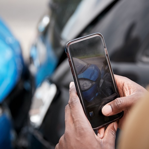 Close inspection of a damaged silver front bumper and fender with a tablet documenting the collision damage