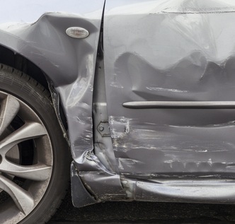 Damaged silver vehicle in an impound yard with valuation paperwork spread across the hood